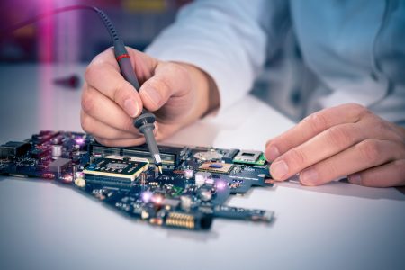 Tech fixes motherboard in service center. Shallow DOF, focus on hands, image is toned with extra light effects